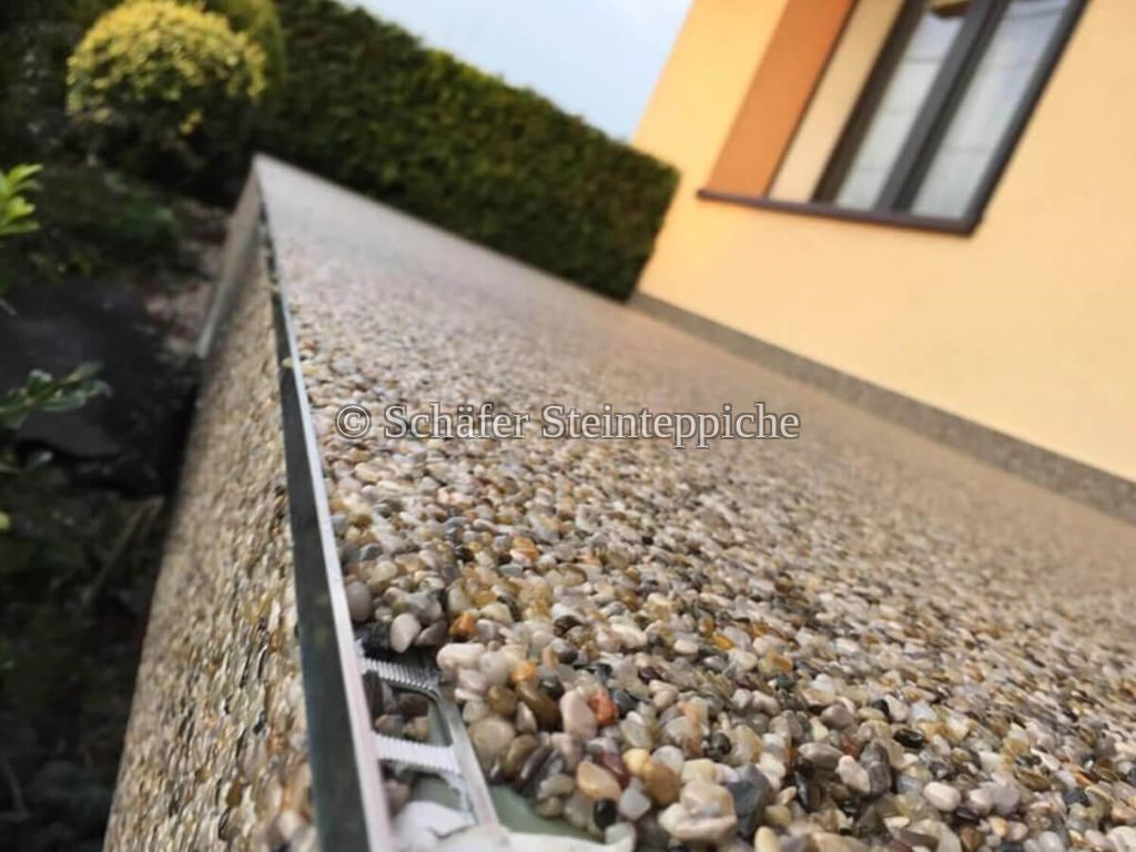Gehweg mit Kies-Steinteppich und sauberer Aluminiumkante entlang einer Hecke